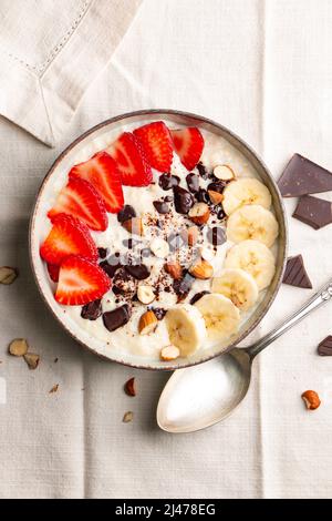 Porridge de millet avec fraise, banane, morceaux de chocolat noir, noisette et amande dans un bol en céramique sur une serviette blanche Banque D'Images