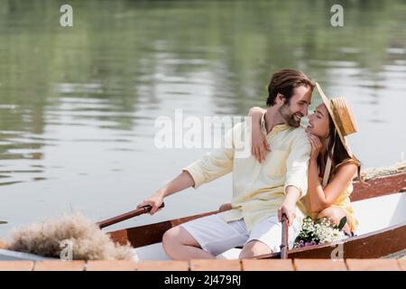 jeune femme gaie en chapeau de paille embrassant l'homme heureux lors d'une excursion romantique en bateau Banque D'Images