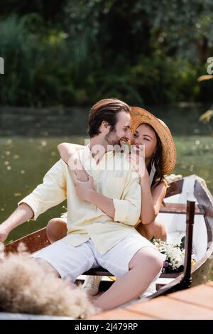 bonne jeune femme en chapeau de paille embrassant homme souriant lors d'une croisière romantique Banque D'Images