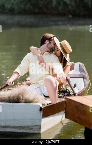 jeune femme en chapeau de paille embrassant l'homme pendant la croisière romantique Banque D'Images