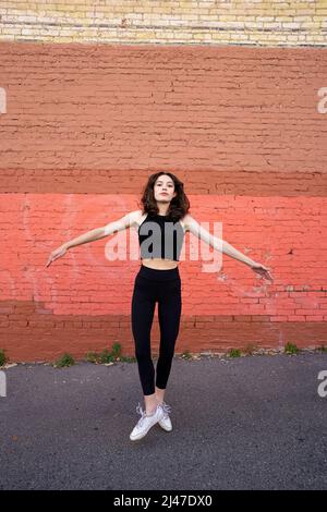 Danseuse adolescente debout près du bâtiment en briques peintes dans le centre-ville de Berkeley Banque D'Images