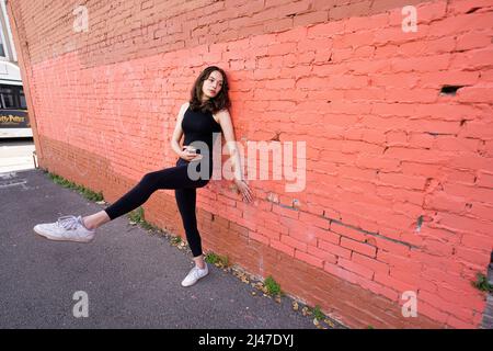 Danseuse adolescente debout près du bâtiment en briques peintes dans le centre-ville de Berkeley Banque D'Images