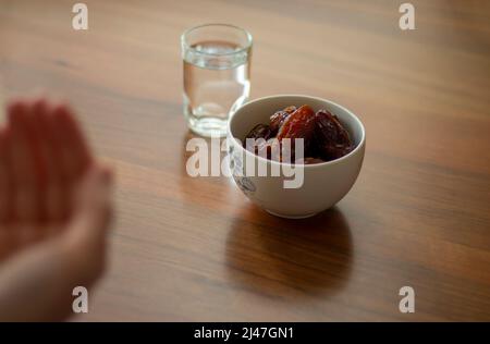 Ramadan ou iftar concept pour les musulmans. La personne prie avec les mains avant de rompre le jeûne. Medjool, eau, repas minimal sur table en bois. Bairam M Banque D'Images