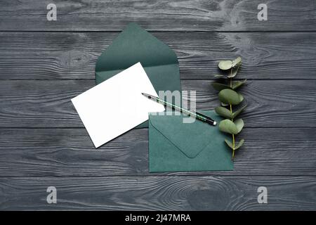 Enveloppes avec carte vierge, stylo et branche d'eucalyptus sur fond de bois foncé Banque D'Images