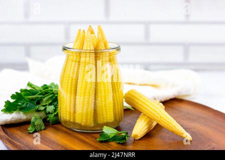 Savoureux de petits épis de maïs jaune sucré bio marinés en boîte dans un pot en verre dans la cuisine. Banque D'Images