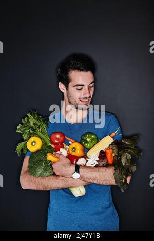 Bien manger pour la santé de lui. Photo en studio d'un jeune homme portant une quantité de légumes sains sur un fond sombre. Banque D'Images