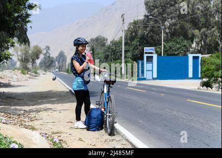 une femme souriante boit de l'eau près d'un vélo après le sport Banque D'Images