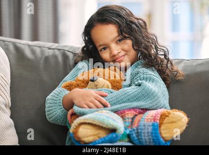 Confort dans un jouet. Photo d'une adorable petite fille assise seule sur le canapé à la maison et tenant un ours en peluche. Banque D'Images