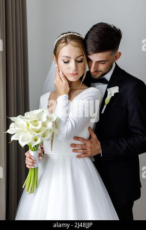 Une jolie mariée habille une mariée dans une robe de mariée. Les jeunes mariés s'embrassent dans la chambre et passent du temps ensemble Banque D'Images