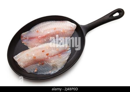 Le filet de poisson blanc, arrosé de gros sel rose, se trouve dans une poêle en fonte. Préparé pour la friture. Isolé sur fond blanc. Vue de dessus avec Banque D'Images