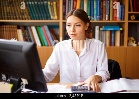 Assistante administrative réfléchie vérifiant des informations de lecture d'ordinateur et notant des données, femme qualifiée regardant la vidéo en ligne pensant à des rapports en ligne, écrivant dans le bloc-notes Banque D'Images