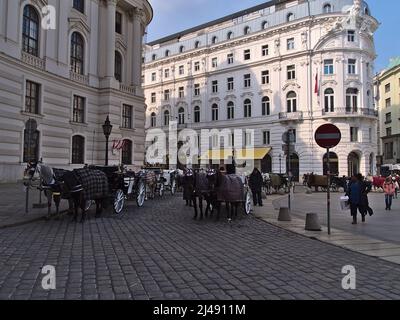 Scène animée sur la célèbre place de la ville de Michaelerplatz, dans le centre historique de Vienne, en Autriche, avec des calèches à cheval qui attendent les touristes. Banque D'Images