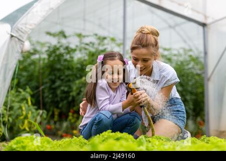 Famille heureuse travaillant dans la serre organique. Femme et enfant cultivons des plantes biologiques dans le jardin de la ferme. Banque D'Images