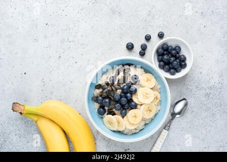 Petit déjeuner porridge bol à flocons d'avoine avec banane, bleuets et graines de pepita sur fond de béton gris. Vue de dessus, espace de copie Banque D'Images