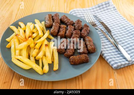 CEVAPi, plat traditionnel de viande hachée des balkans, servi avec des frites dans une assiette bleu marine sur une table en bois Banque D'Images