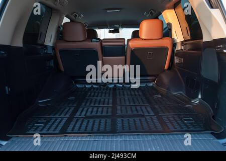 Le grand coffre vide noir de voiture de vus avec tapis en caoutchouc et dossier en cuir sur le plancher porte-bagages ouvert de la voiture de proximité Banque D'Images