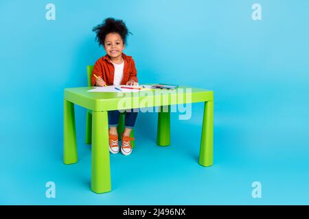 Photo pleine longueur de mignonne ondulée petite fille vêtements de peinture chemise jeans baskets isolées sur fond bleu Banque D'Images