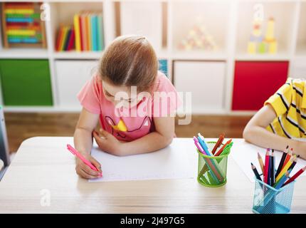 Écolière en classe assise aux tables et écrivant une leçon. Banque D'Images