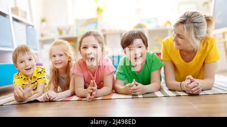 Groupe d'enfants et d'enseignants allongé sur le sol et regardant dans l'appareil photo. Banque D'Images