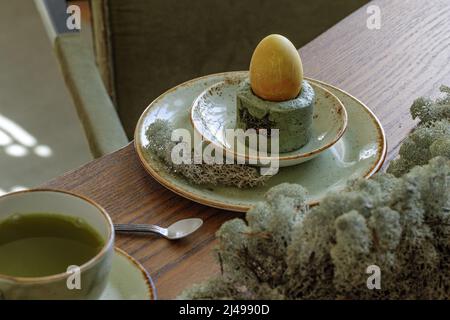 Table pour le dîner de Pâques décorée de mousse forestière, œufs colorés avec du thé matcha dans un plateau de ciment vert mousse. Table en chêne massif contre du texte en argile Banque D'Images