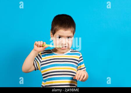 Magnifique enfant heureux en T-shirt rayé brosses dents avec une brosse à dents verte sur fond bleu, espace de copie pour le texte. Banque D'Images
