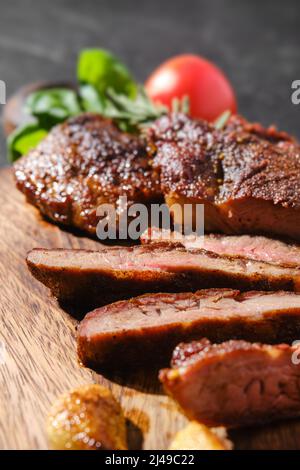 Vue rapprochée de l'araignée de beefsteak frite dans une poêle en fonte, servie sur un plan de coupe en bois avec tomate et basilic Banque D'Images