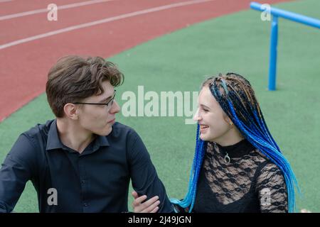 Une jeune femme heureuse et un jeune homme. Rire de couple hétérosexuel dans l'amour dehors. Drôle de jeunes adultes. Femme avec des dreadlocks bleus. Homme portant des lunettes Banque D'Images