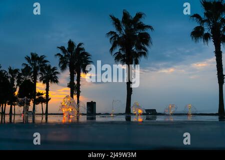 Magnifique coucher de soleil en soirée sur la rive de la mer avec fontaines, palmiers. Paysage de ville charmant Banque D'Images