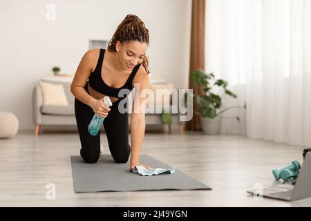 Black Fitness Woman Cleaning Gym Mat avant l'entraînement à la maison Banque D'Images