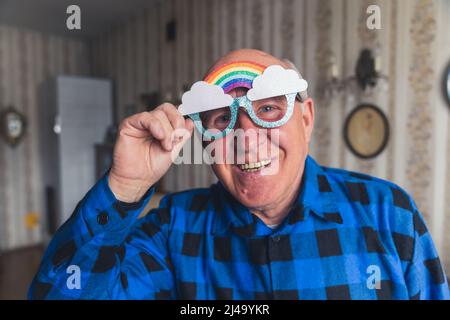 Drôle de cachique chauve grand-père regardant la caméra et souriant tout en portant des lunettes funky arc-en-ciel. Intérieur vintage. Photo de haute qualité Banque D'Images