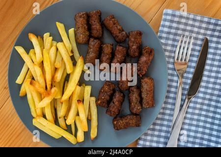 CEVAPi, plat traditionnel de viande hachée des balkans, servi avec des frites dans une assiette bleu marine sur une table en bois Banque D'Images