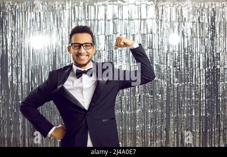 Heureux confiant jeune homme noir en costume souriant et fléchissant son bras avec des muscles forts Banque D'Images