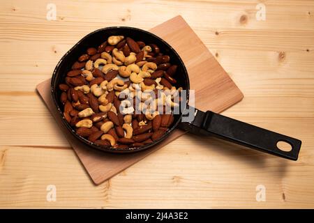 Amandes grillées et noix de cajou dans une casserole sur une planche de bois Banque D'Images