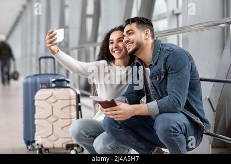 Un jeune couple arabe heureux prend Selfie sur un smartphone à l'aéroport Banque D'Images
