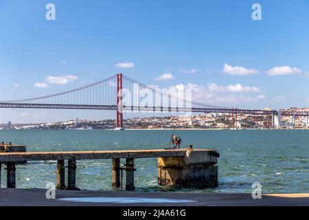 Pêche de pêcheur dans le Tage sous pont suspendu avec le paysage urbain de Lisbonne en arrière-plan, Portugal, Europe Banque D'Images