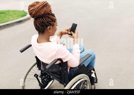 Jeune femme noire en fauteuil roulant utilisant un téléphone portable avec maquette pour l'application mobile en plein air Banque D'Images