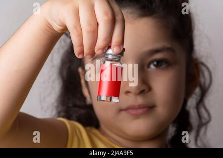 Petite fille tenant un flacon d'injection devant le visage. Modèle de série de maquettes modifiable prêt pour votre conception. Chemin de sélection d'étiquette de bouteille inclus. Banque D'Images