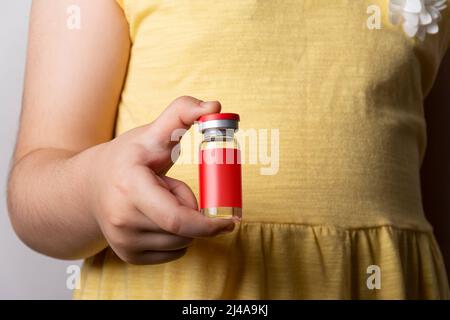 Petite fille tenant un flacon d'injection dans la main droite. Modèle de série de maquettes modifiable prêt pour votre conception. Chemin de sélection d'étiquette inclus. Banque D'Images