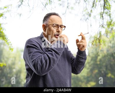 Homme mature fumant et toussant à l'extérieur dans un parc Banque D'Images