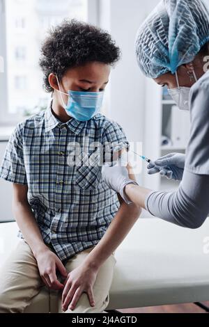 Enfant dans le masque recevoir le vaccin de l'infirmière lors d'une visite au bureau pédiatrique Banque D'Images