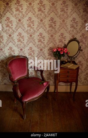 Cette chambre vintage comprend un fauteuil en velours, un miroir ancien, des roses roses roses et un livre ancien Banque D'Images