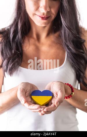 Brunette femme tenant un coeur ukrainien soigneusement dans ses mains en fron de sa poitrine. Représentant l'amour et l'emphaty aux personnes attaquées. Dos isolé Banque D'Images