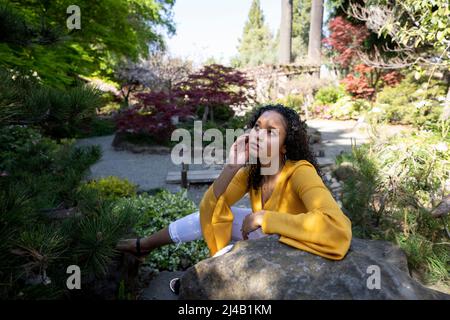 Belle jeune femme noire assise sur Rocks dans un jardin japonais Banque D'Images