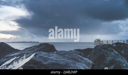 Vieux cabanes de pêche en bois typiques sur pilotis appelées « carrelet » dans l'océan atlantique près de la Rochelle, France. Prises au coucher du soleil par un jour de tempête. Banque D'Images