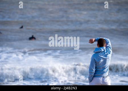 Vue arrière d'un jeune homme sur la plage de Rivedoux en regardant les surfeurs monter sur les vagues, Ile de Ré, Ile de Ré, Ile de Ré, France. Banque D'Images