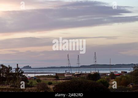 Bateaux à voile « beached » avec des oiseaux perchés dans leur gréement et le château de Bamburgh à l'horizon à l'aube Banque D'Images