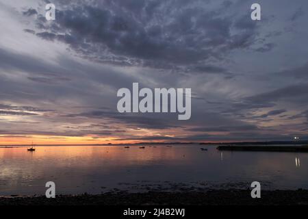 Voiliers et bateaux à moteur amarrés dans le port de l'île Sainte à des moments de marée haute avant le lever du soleil dans un ciel rouge, jaune et orange vif. Banque D'Images