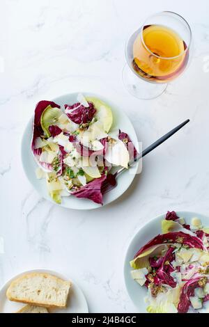 Salade au radicchio, chicorée et parmesan servie avec un verre de vin orange sur fond blanc Banque D'Images