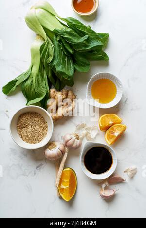 Ingrédients pour cuisiner un plat de cuisine asiatique sur une table en marbre. Bok choy frais, tranches d'orange et condiments. Banque D'Images