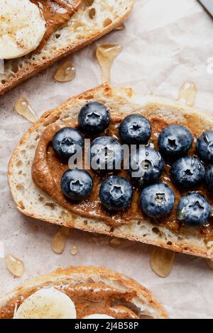 Pain grillé au levain, servi avec du beurre d'amande, des bleuets, de la banane et un filet de miel. Banque D'Images